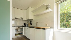 A modern kitchen with white cabinets, a stove, and a window with a view of greenery. - Beautiful home with roof terrace and a view of the water. (Oude-Tonge)