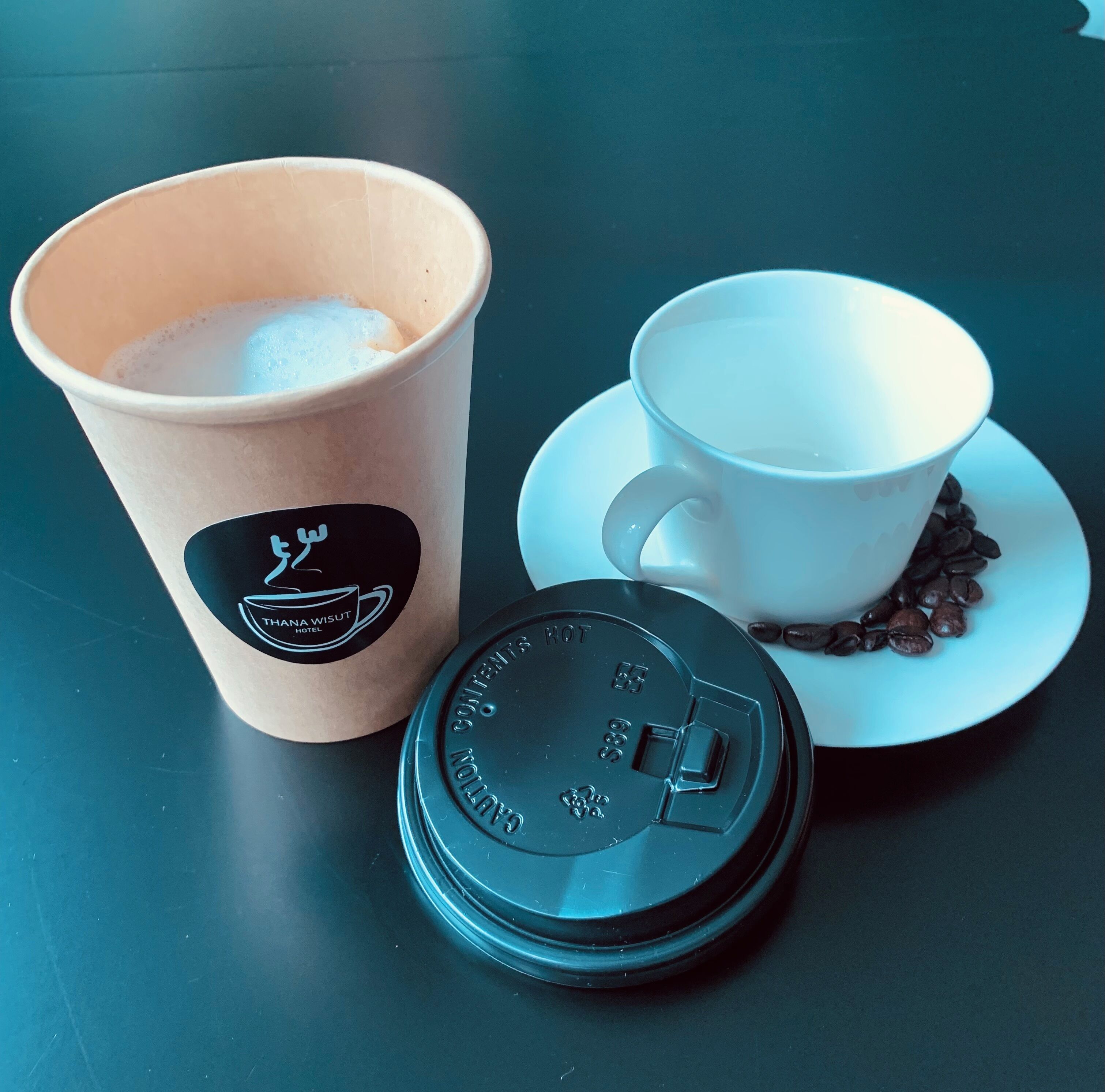 A coffee cup with a logo, a white cup with a saucer, and a lid on a table.