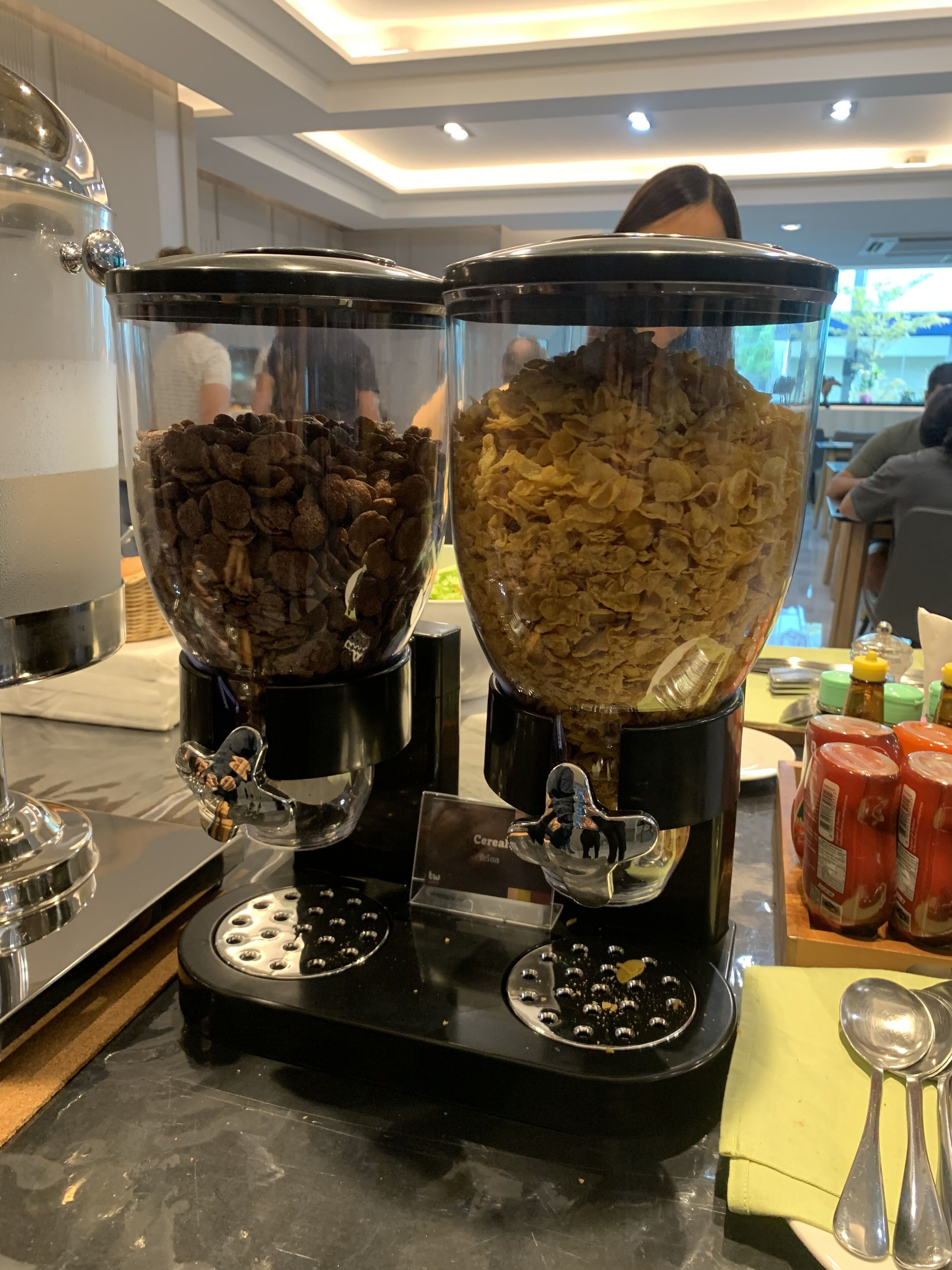 A breakfast bar with two large bowls of cereal, a coffee machine, and condiments.