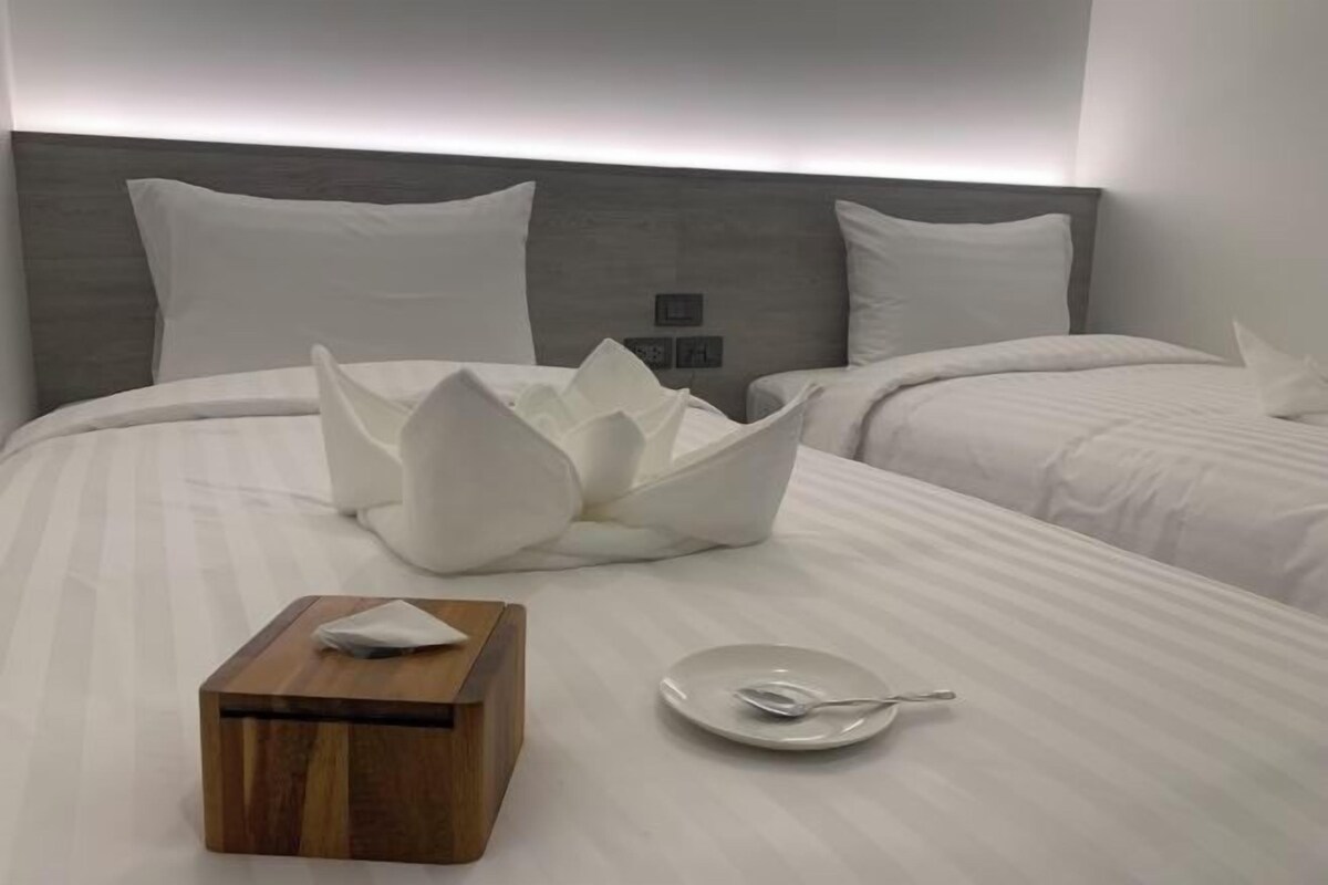 A hotel room with a neatly made bed, a bedside table with a tissue box and a plate, and a modern headboard.