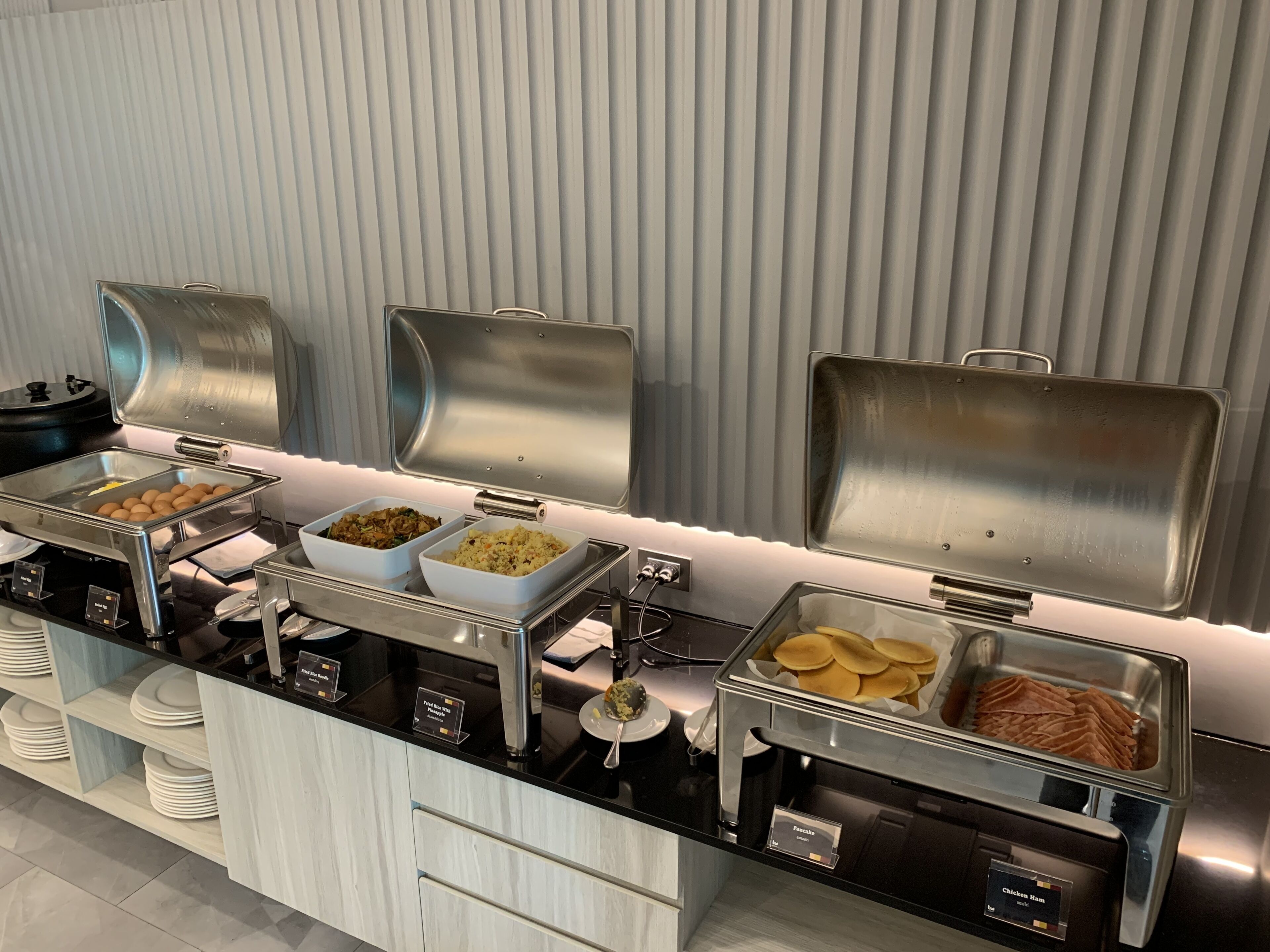 A buffet setup with various food items in metal containers, including eggs, salads, and pancakes.