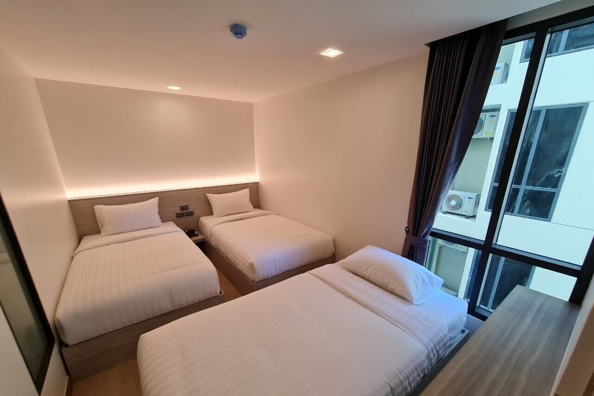A hotel room with three beds, a large window with curtains, and a ceiling light.