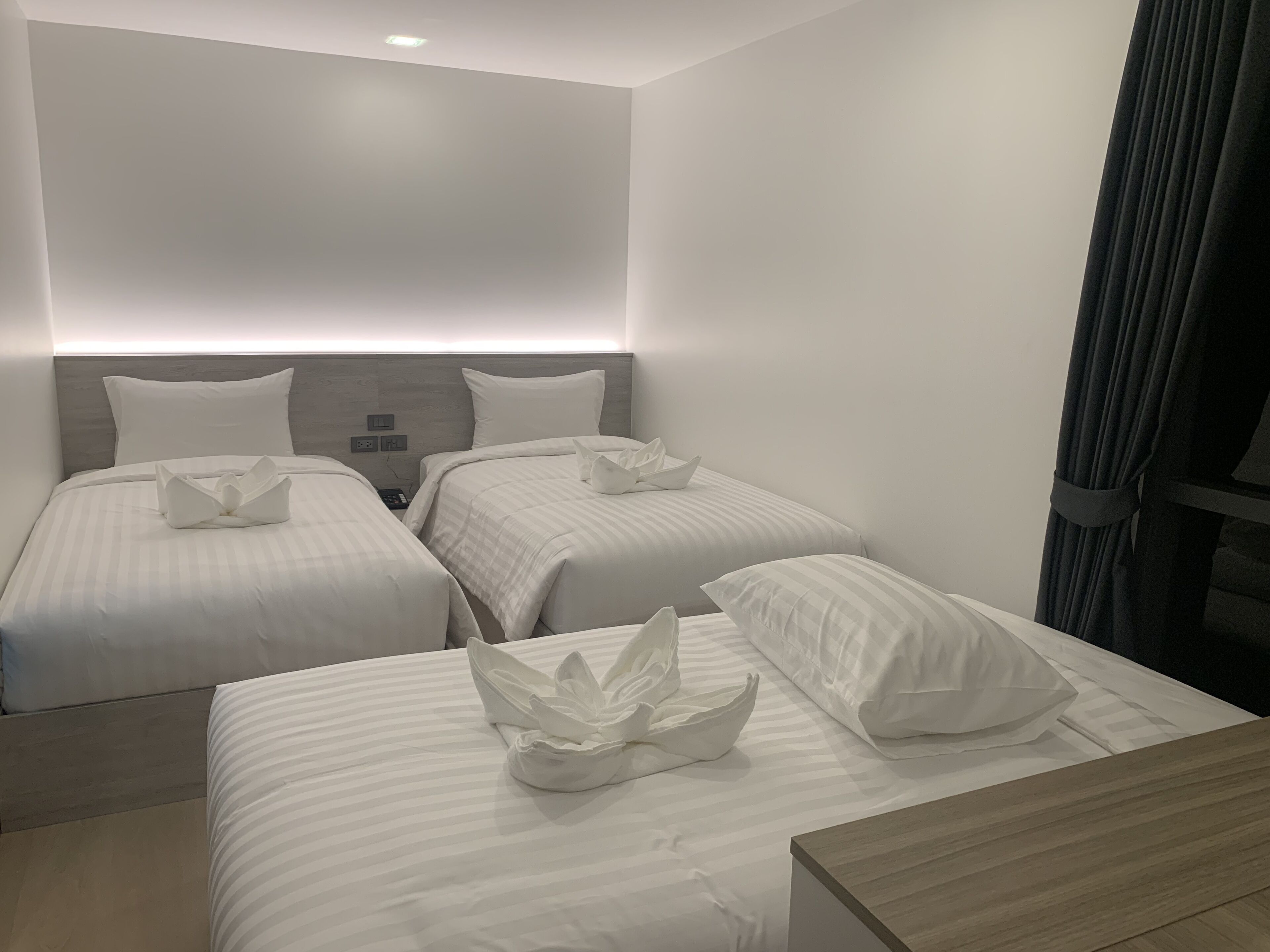 Hotellihuone, jossa on kaksi sänkyä. Jokaisessa sängyssä on valkoinen tyyny ja koriste-esine. Etualalla on puinen yöpöytä.