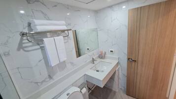A modern bathroom with a marble backsplash, a white sink, a mirror, and a wooden door.