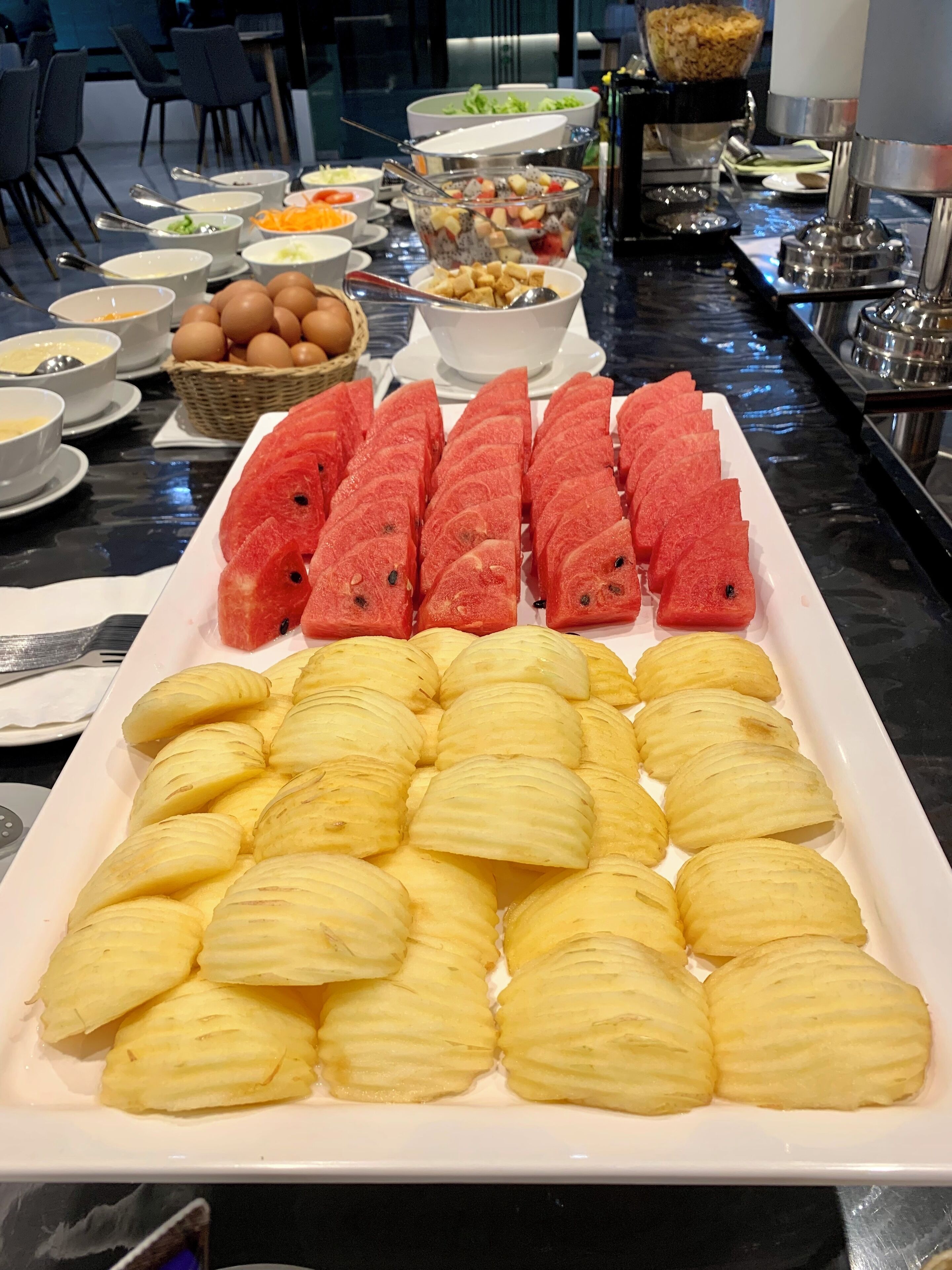 A buffet table with various dishes including watermelon slices, pineapple chunks, and other food items.