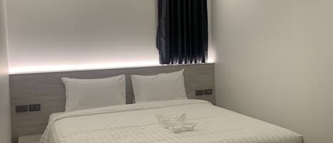 Una habitación de hotel moderna con una cama grande, cabecera con iluminación integrada, cortina oscura y cámara de seguridad en el techo.