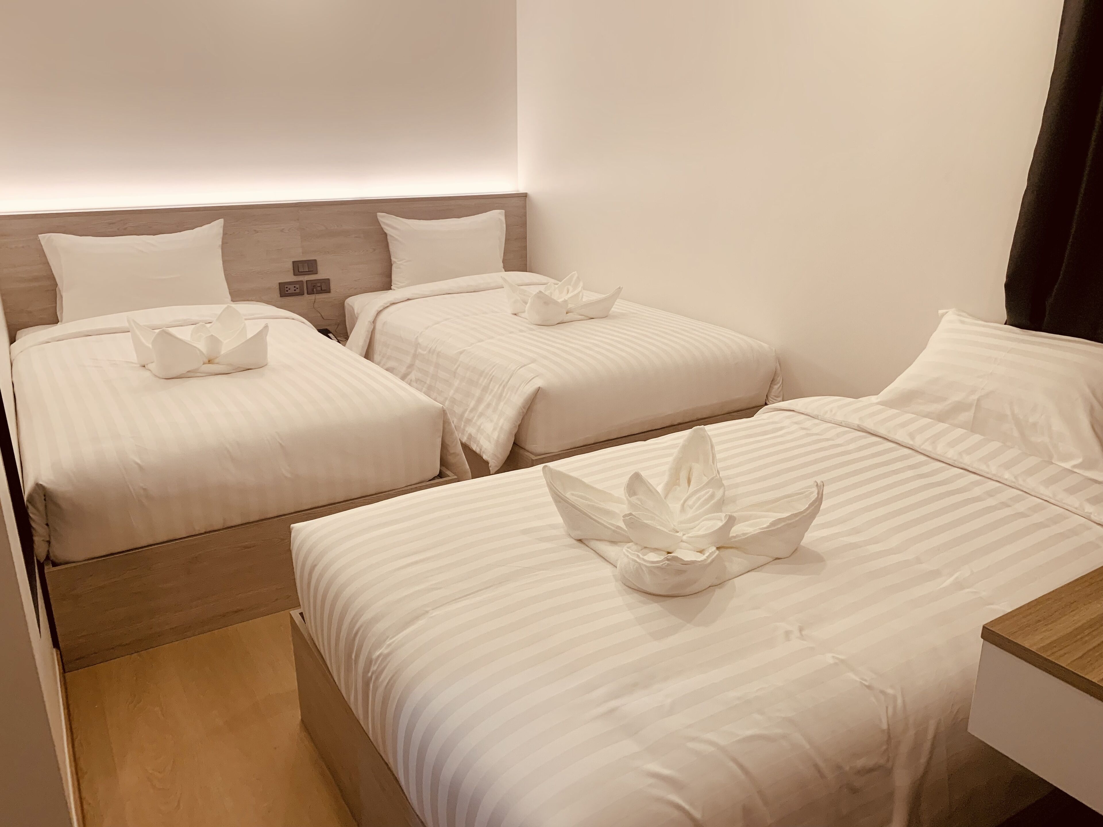 Ein Hotelzimmer mit drei Betten, jeweils mit weißer Bettwäsche und einem Holzkopfstück.