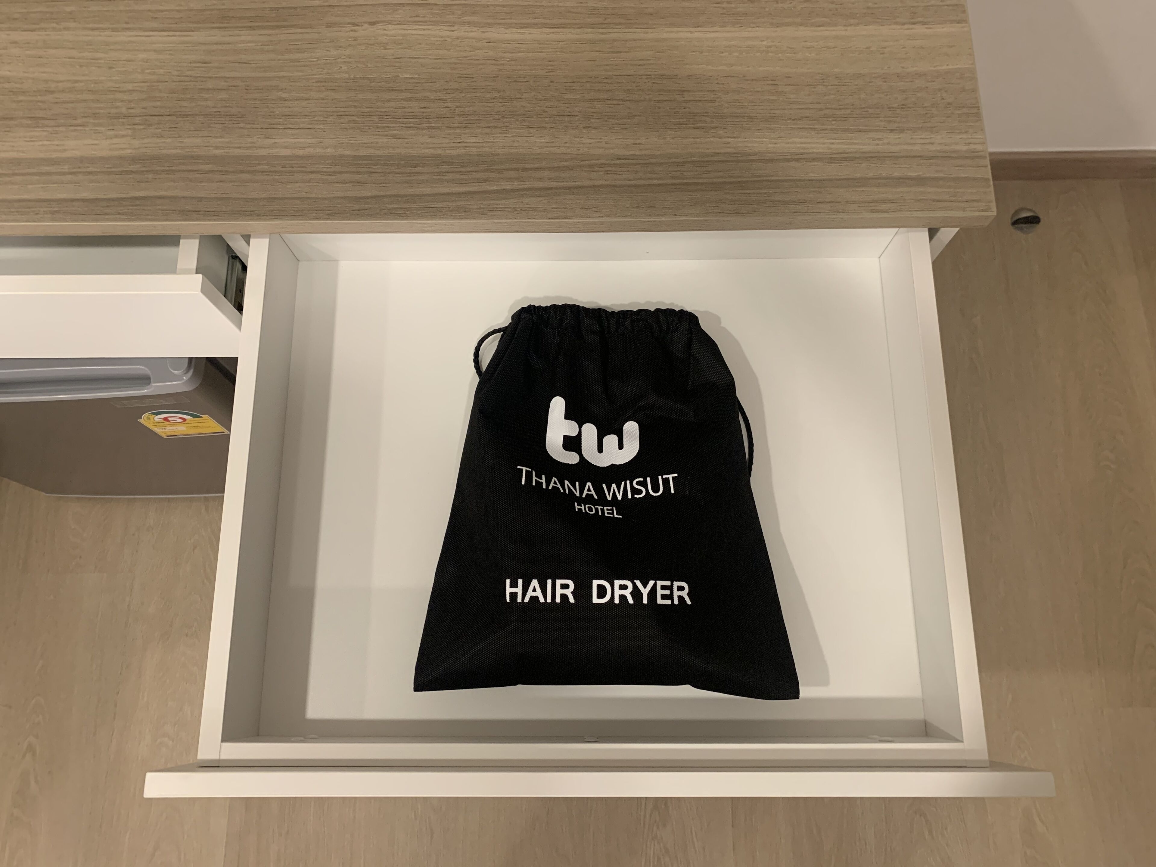 A black drawstring bag labeled "THANA WISUT HOTEL HAIR DRYER" in a white drawer.