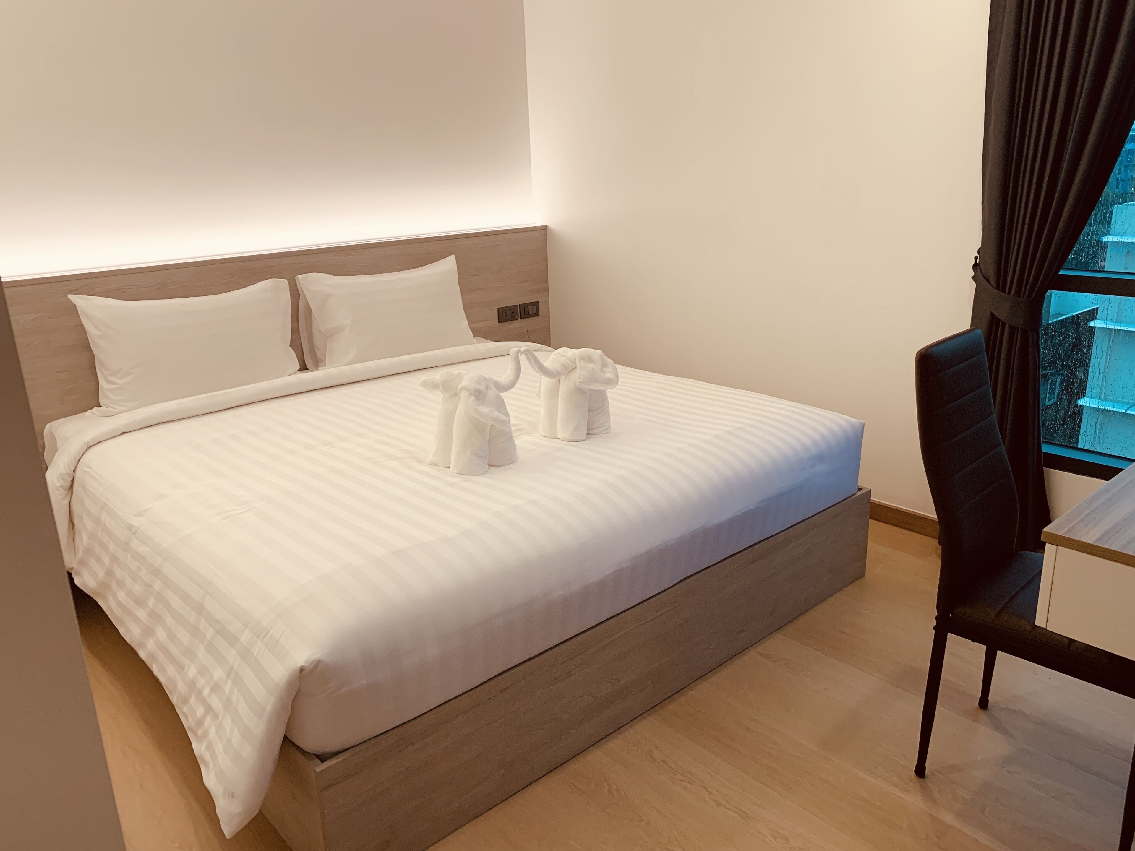 A neatly made bed with a wooden headboard, two white pillows, and two towels arranged in a bow shape.