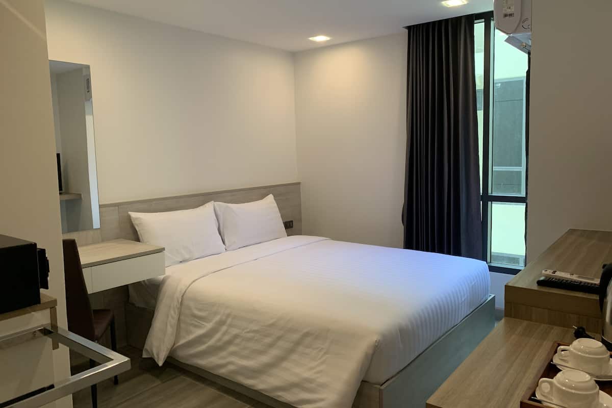 A hotel room with a bed, a desk, a chair, a TV, a window with curtains, and a tray with cups and saucers.