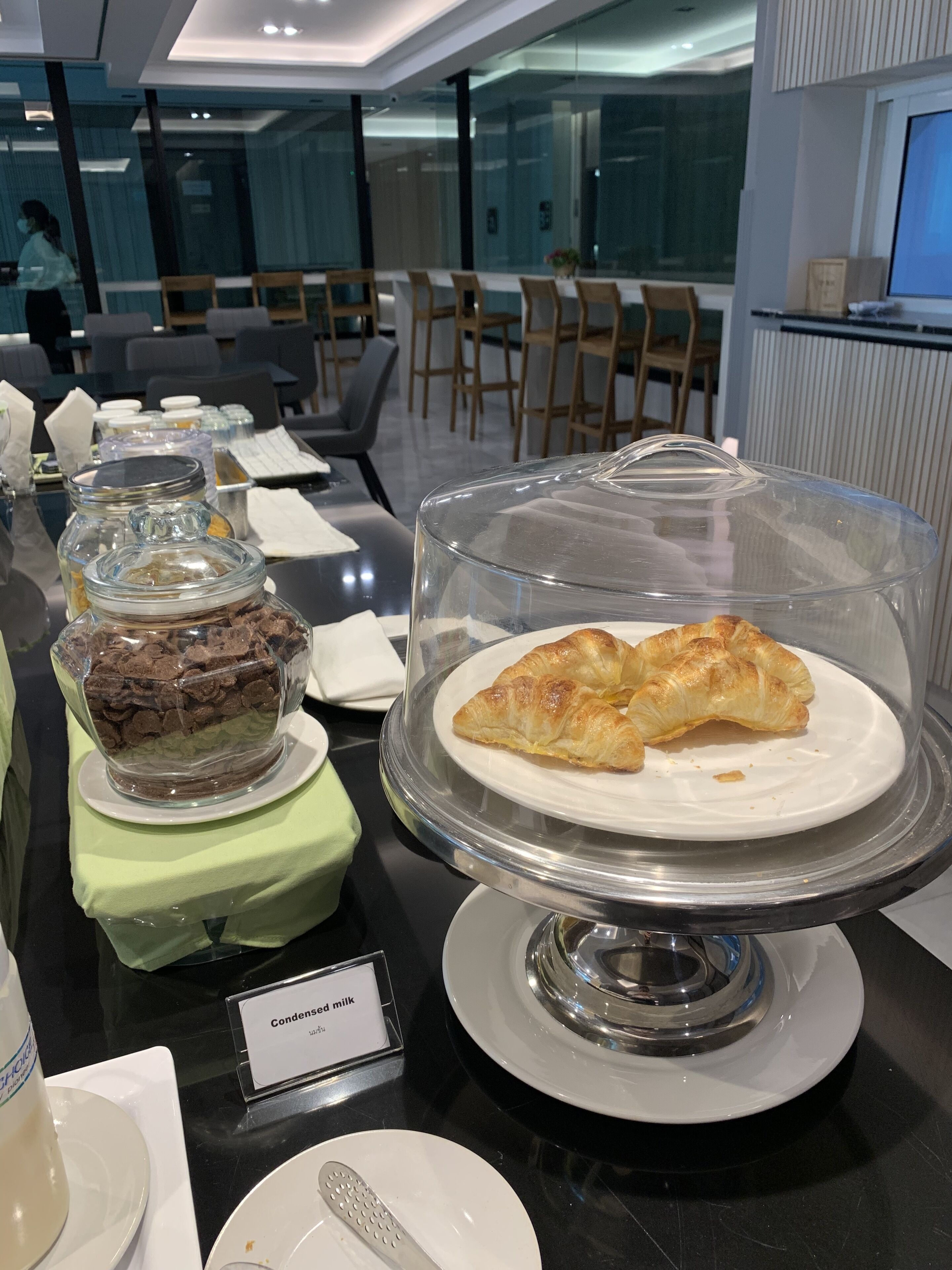 A buffet with a variety of food items including a glass-covered dessert stand with pastries and a label indicating condensed milk.