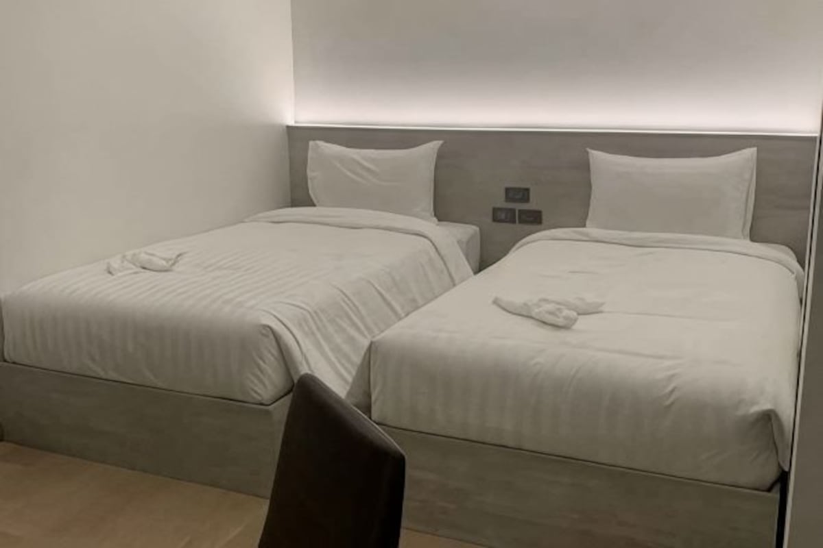 Two twin beds with white linens, a chair, and a wall-mounted light fixture.