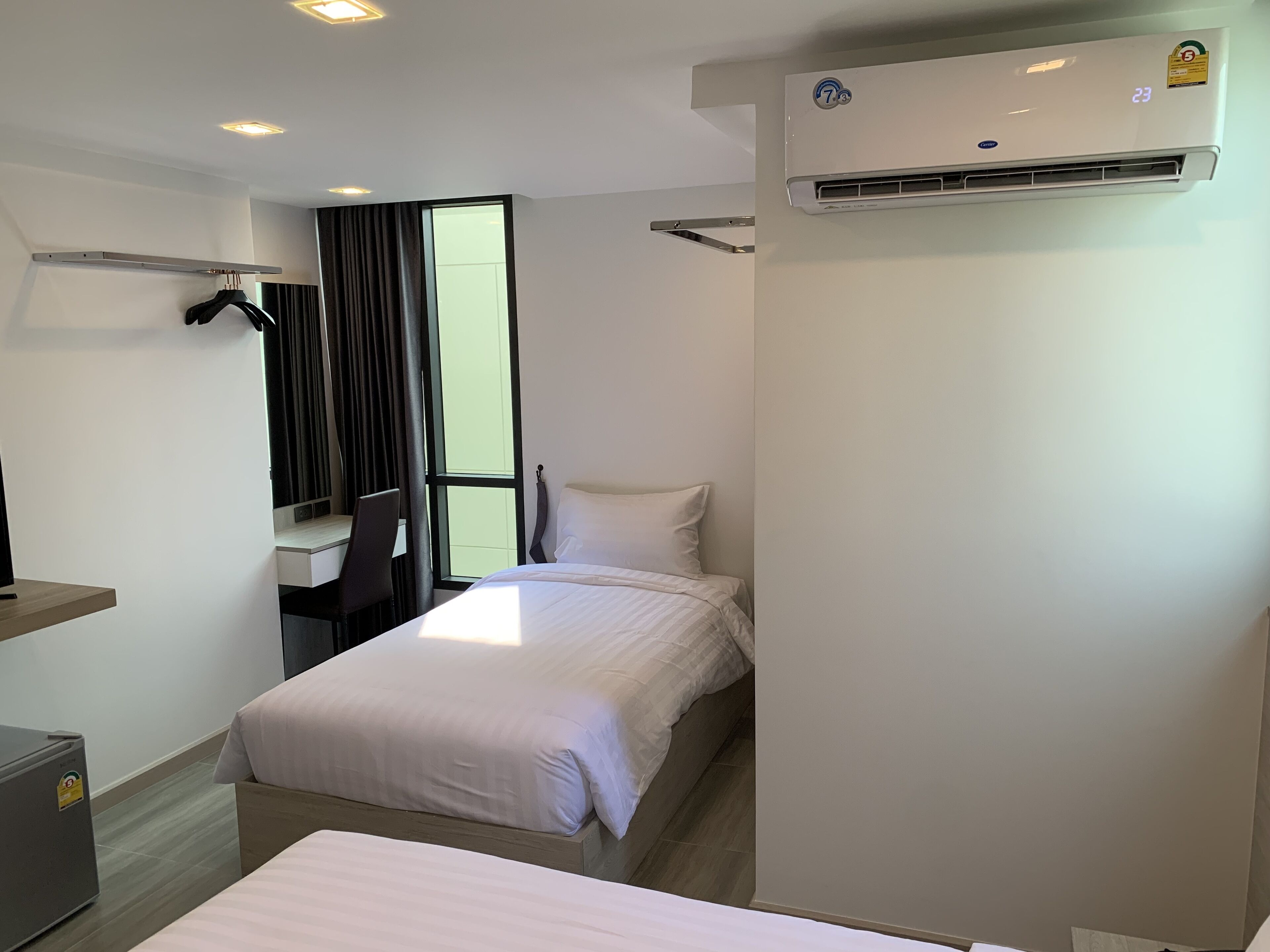 A hotel room with a bed, a desk, a chair, an air conditioning unit, and a window with curtains.