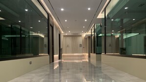 A modern hallway with glass walls, a polished floor, and recessed lighting. - Thana Wisut Hotel (Bangkok)