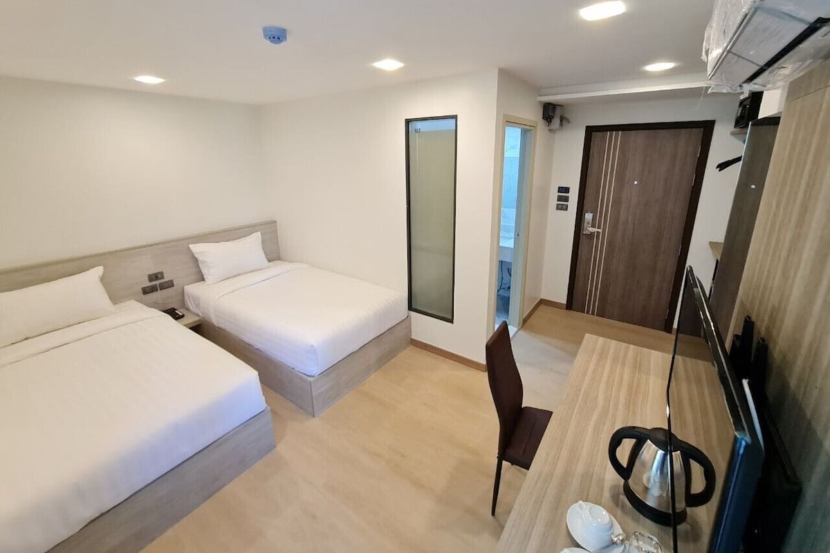 A hotel room with two beds, a desk with a chair, a mirror, and a door leading to another room.