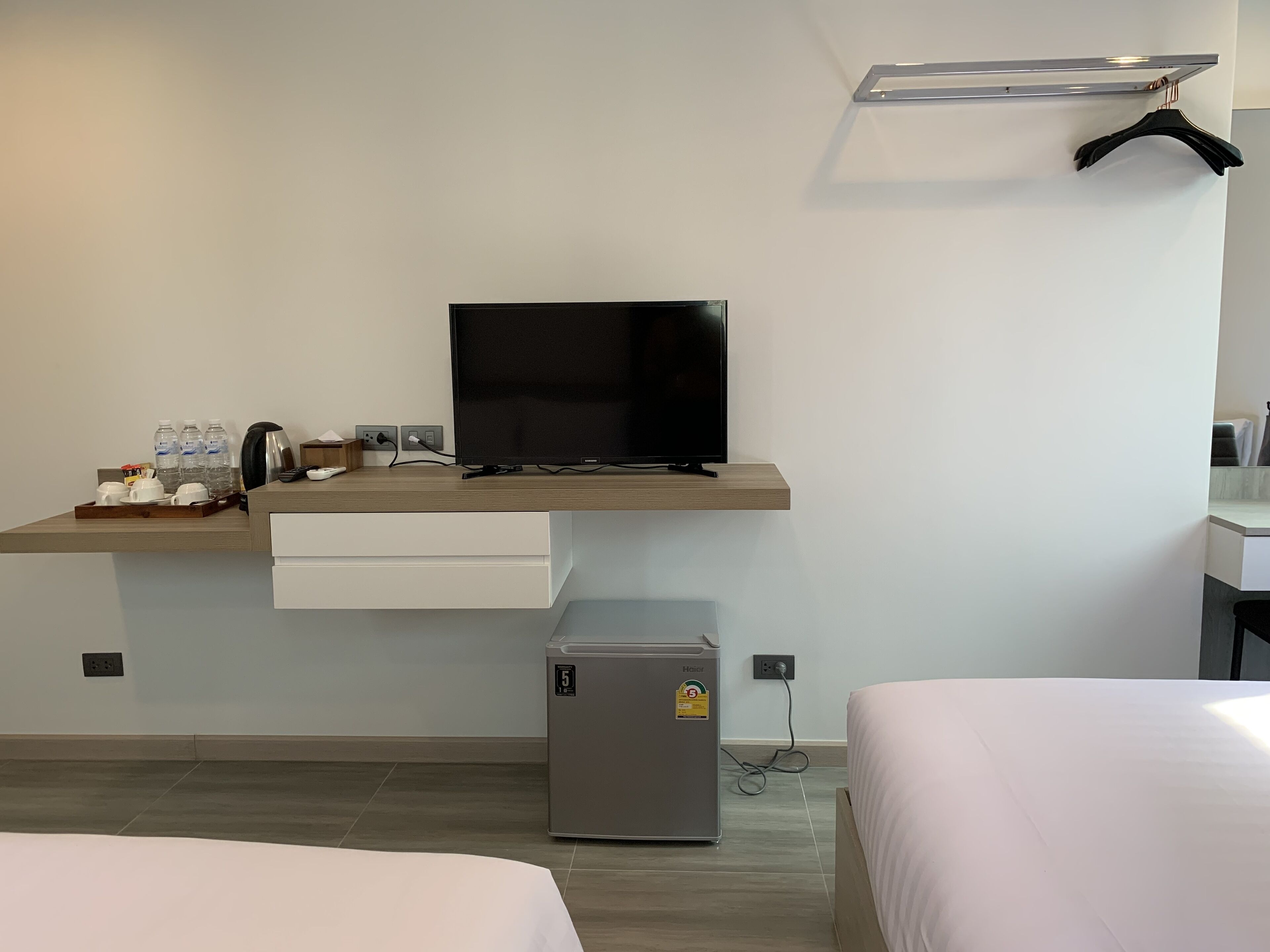 A hotel room with a bed, a desk with a television, a mini-fridge, and a coat rack.