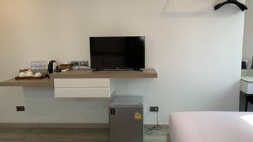 A hotel room with a bed, a desk with a television, a mini-fridge, and a coat rack.