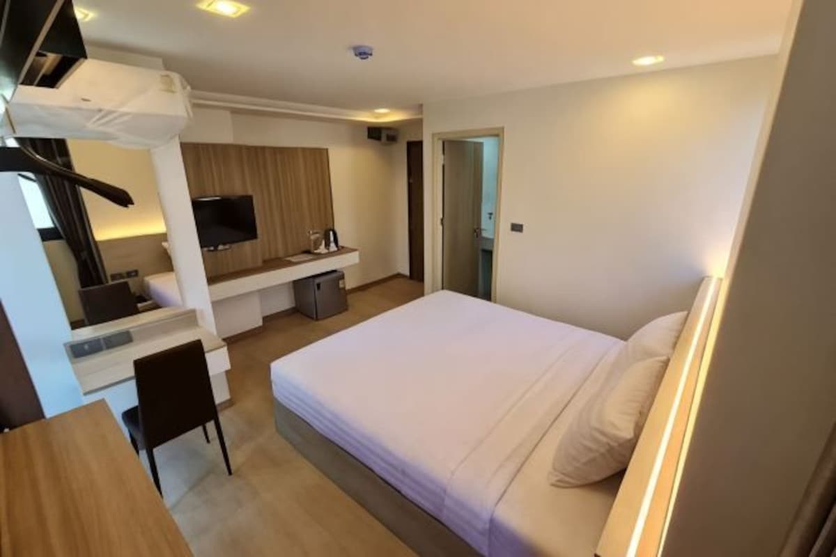 A hotel room with a bed, desk, chair, television, and a small kitchenette.