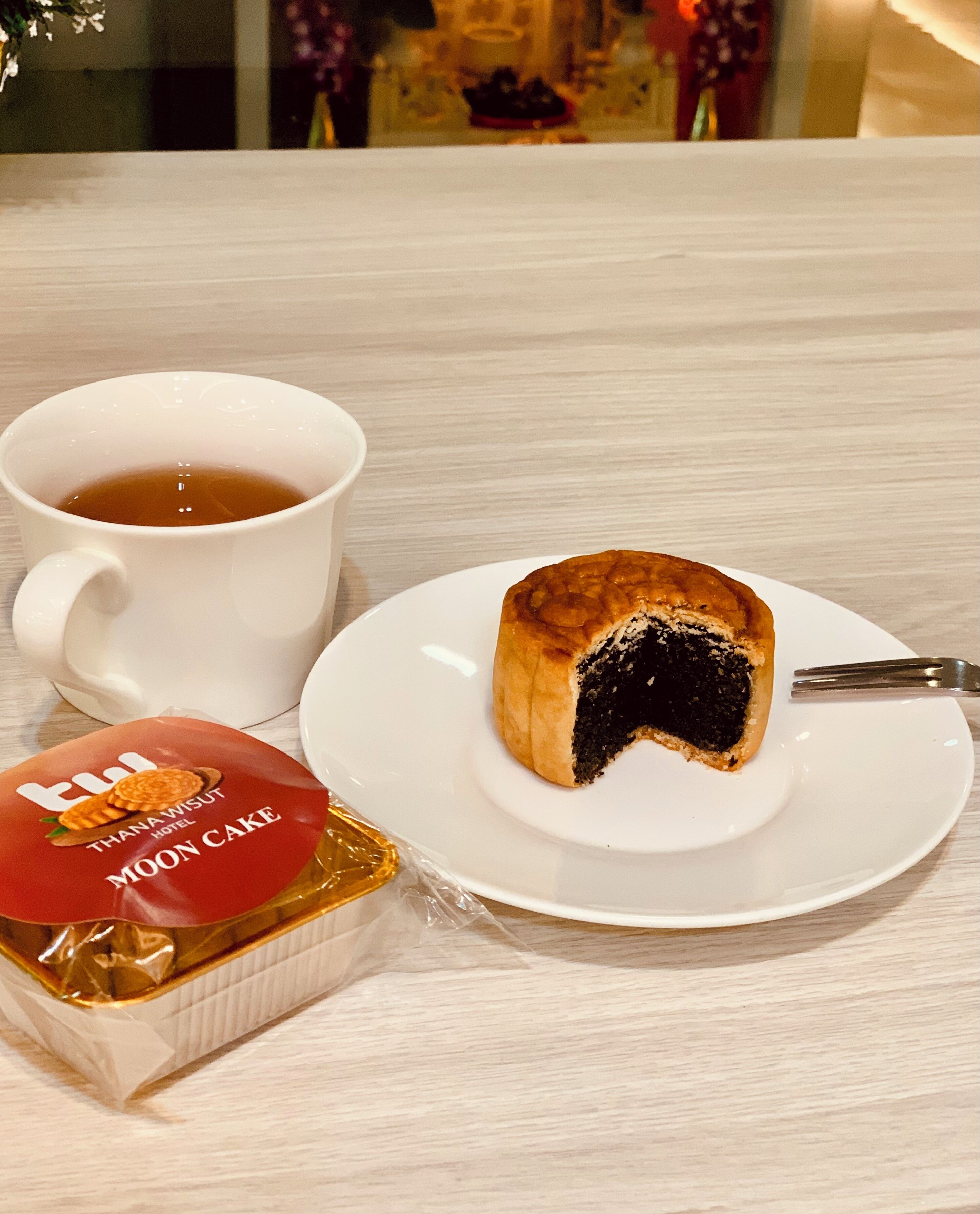 A white cup of tea, a slice of moon cake on a white plate, and a packaged moon cake on a table.