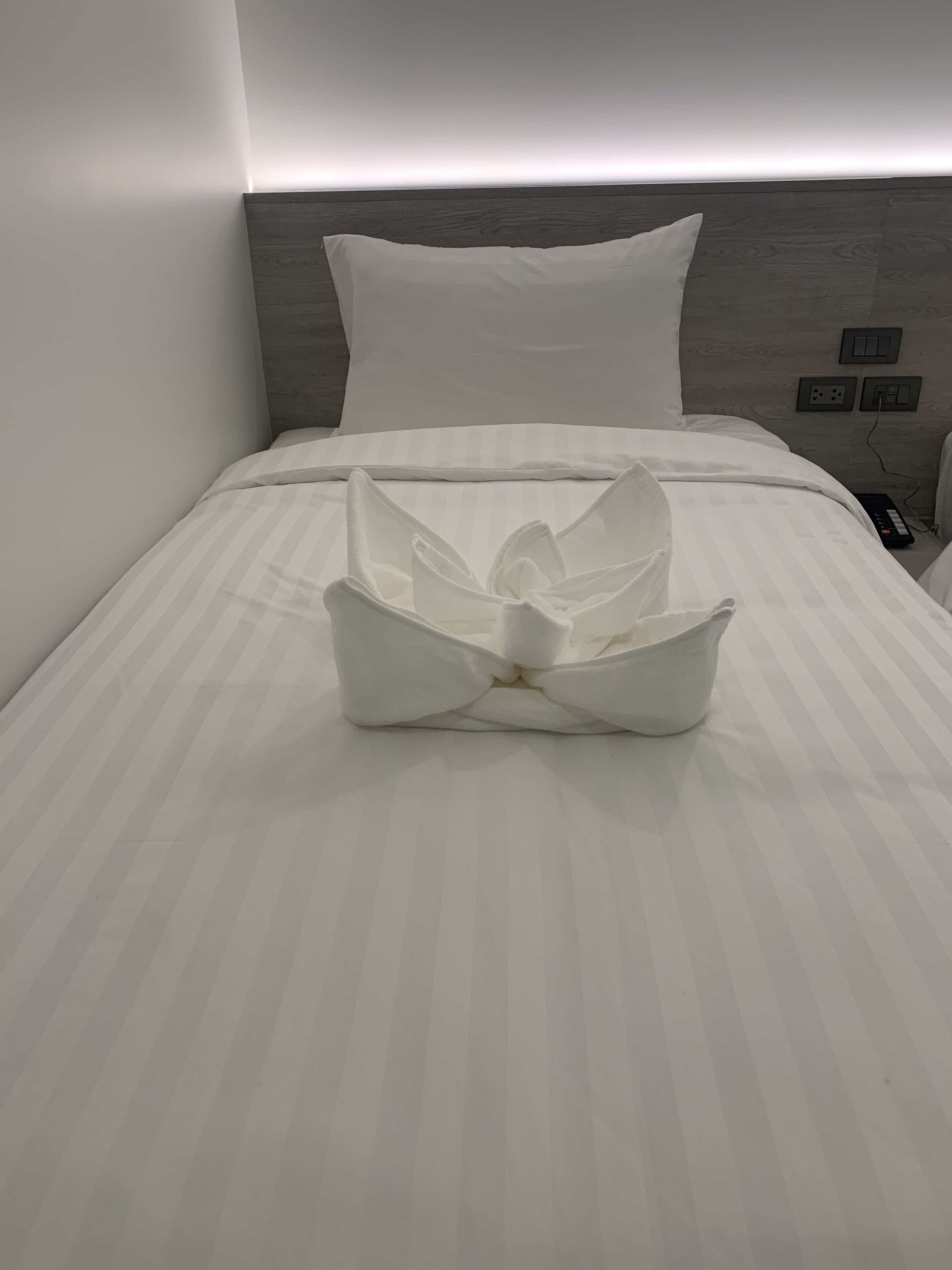 Een net opgemaakt bed met een wit kussen en een groot, wit sprei met bloemmotief.