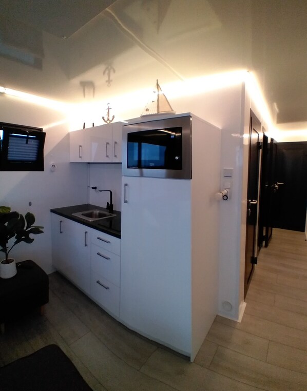 Una cocina compacta con armarios blancos, un microondas integrado y un lavamanos.