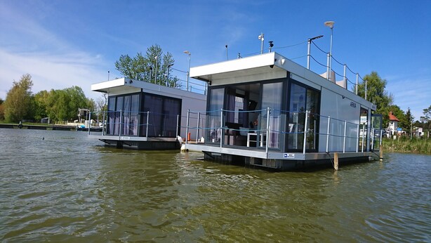 Two floating houses with glass windows and a deck, connected by a bridge, on a calm river. - Domki na wodzie ARKA 1, rower wodny, do morza oraz centrum 400m (Mielno)