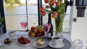 A table with food and drinks, a vase of tulips, and a view of a river. - Domki na wodzie ARKA 1, rower wodny, do morza oraz centrum 400m (Mielno)