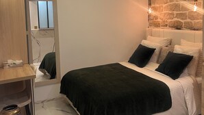 Une chambre à coucher avec un lit, une table de chevet en bois, un miroir et un mur en pierre.
