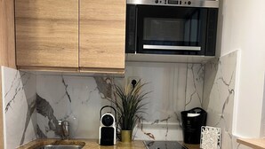Une cuisine compacte avec des meubles en bois, un four à micro-ondes encastré, un petit réfrigérateur et un pare-feu en marbre.