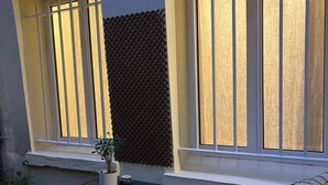 Une terrasse avec une table et des chaises, un pot de fleurs et une fenêtre dont le mur arrière présente une texture particulière.