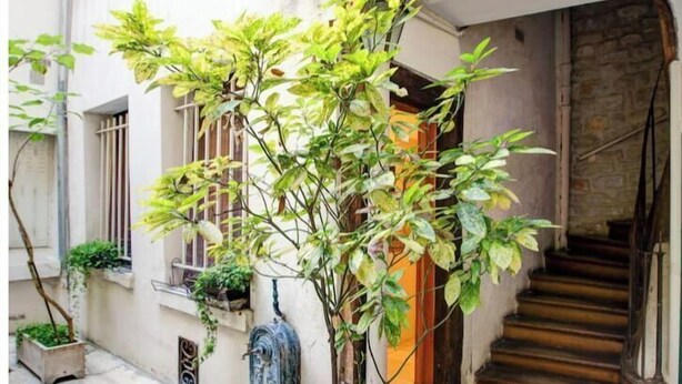 Une ruelle étroite, avec un arbre en pot, une petite statue et un escalier menant à l’entrée d’un immeuble.