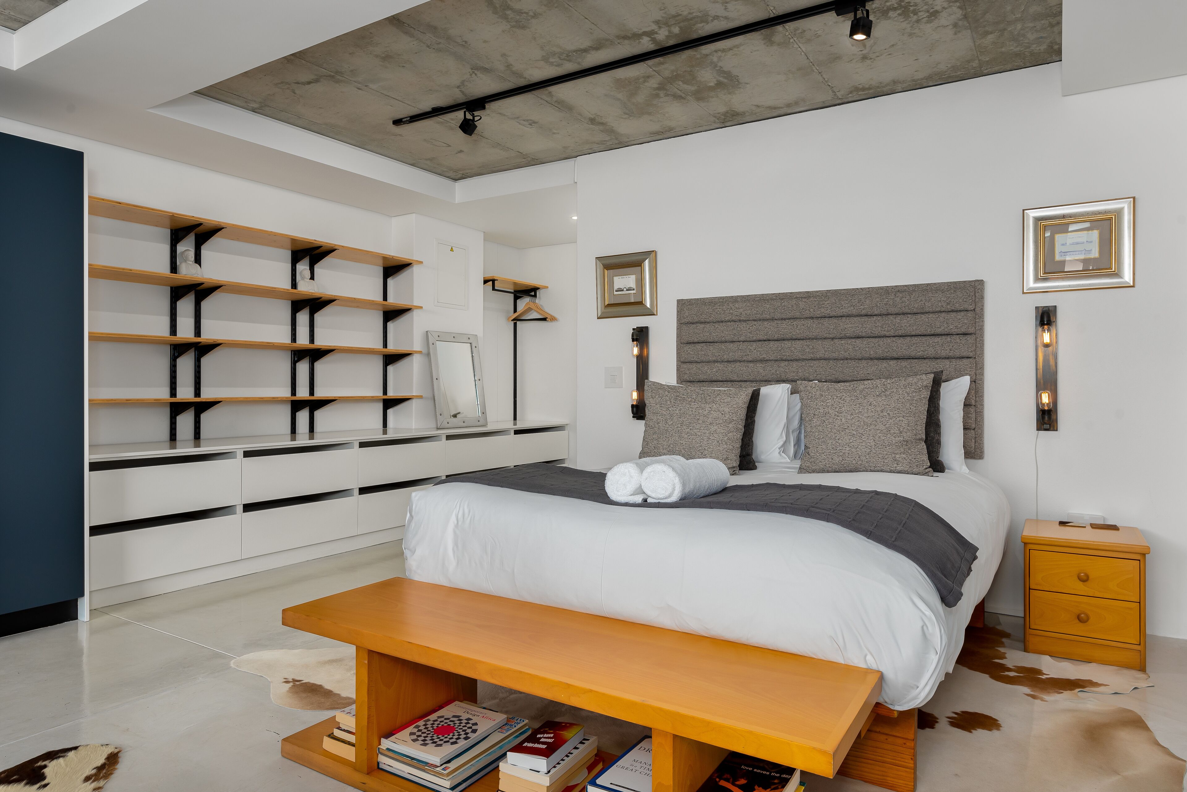A modern bedroom with a large bed, bedside tables, a wooden bench, and built-in shelving.