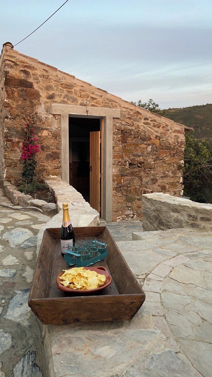 A stone building with a wooden door, a bottle of wine, glasses, and chips on a wooden tray outside.