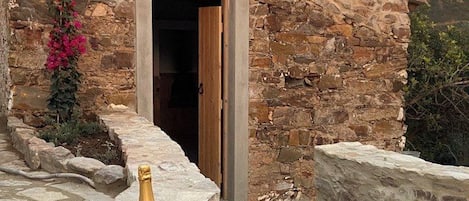 A stone building with a wooden door, a bottle of wine, glasses, and chips on a wooden tray outside.