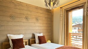 Een hotelkamer met twee bedden, houten paneelwanden, decoratieve wandklokken, een raam met uitzicht op gebouwen en een kroonluchter.