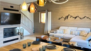 Een moderne woonkamer met een houten wand, een bank, een televisie en een eethoek met een tafel gedekt voor twee personen.
