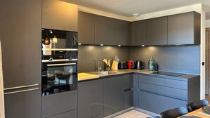 Een moderne keuken met inbouwapparatuur, een eethoek met een houten tafel en stoelen, en een hanglamp.