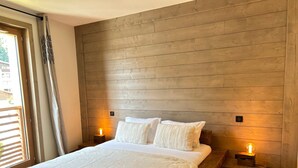 Een slaapkamer met een houten hoofdbord, een groot bed met witte lakens, twee bedlampen en een raam met jaloezieën.