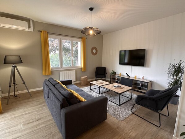 Un salon moderne comprenant un canapé, deux fauteuils, une table basse, un téléviseur et un lampadaire.