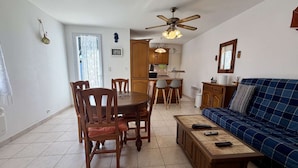 A living room with a sofa, a dining table with chairs, a kitchen area, and a ceiling fan.