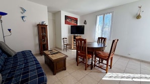 A living room with a sofa, a dining table with chairs, a TV, and a window with curtains.