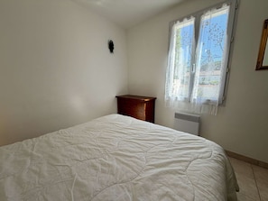 A bedroom with a bed, a wooden nightstand, a radiator, and a window with lace curtains.