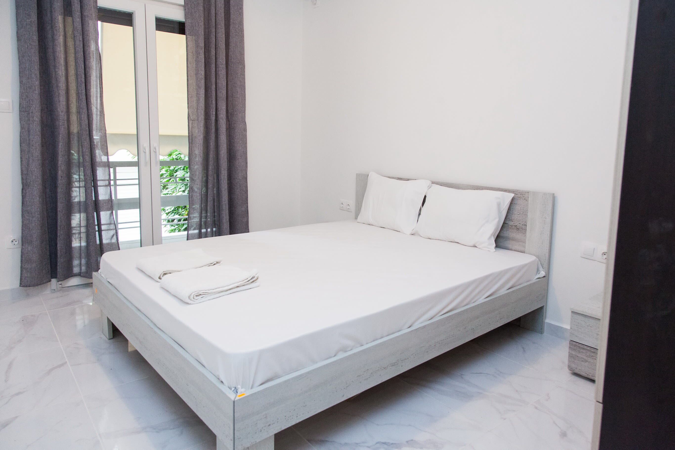 A modern bedroom with a bed, a view through the window, and a door.
