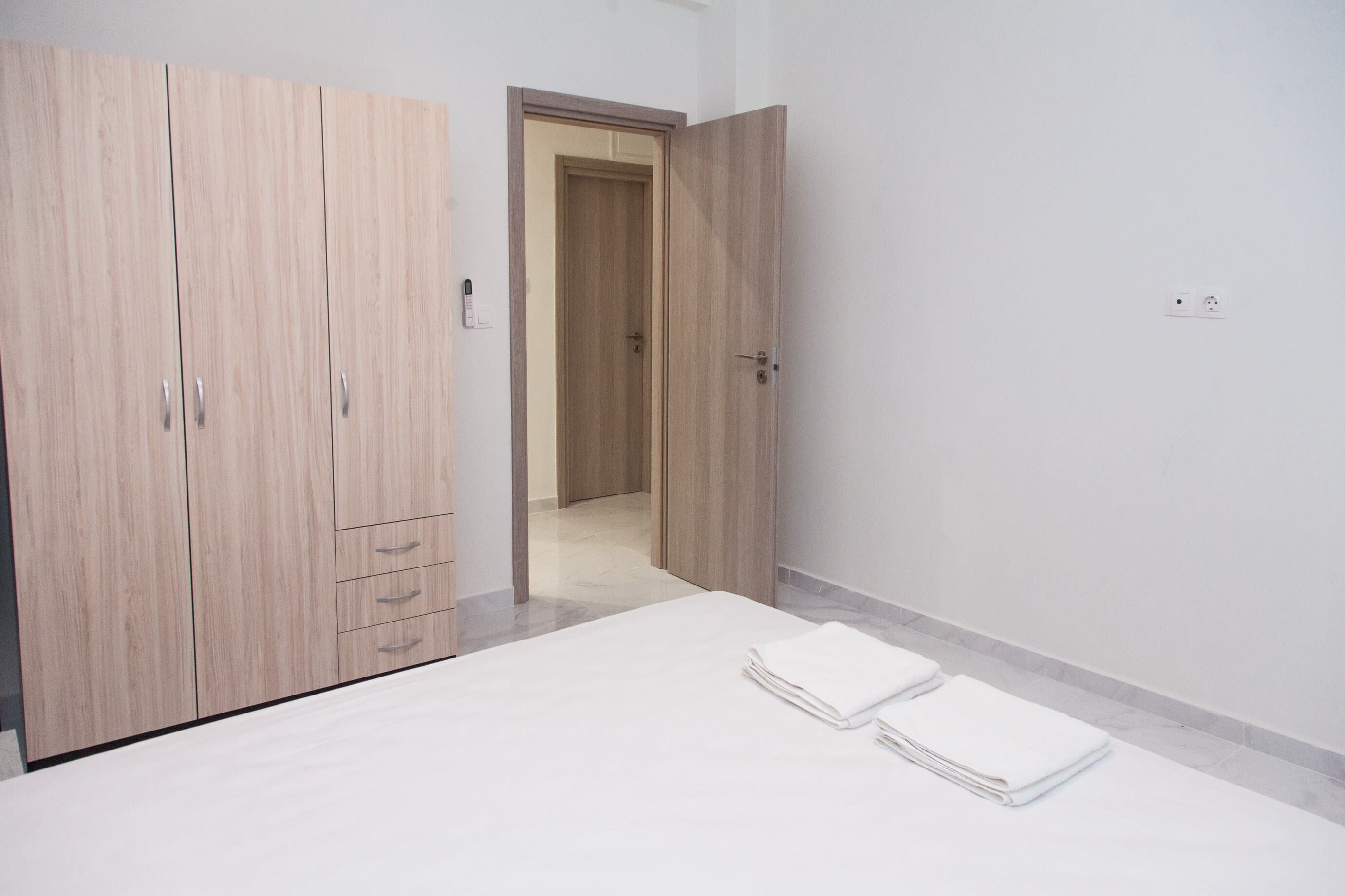 A bedroom with a bed, two white towels, a wooden wardrobe, and a door leading to another room.