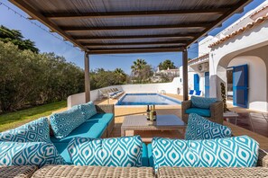 Un área de estar al aire libre techada con piscina, mobiliario de mimbre y vistas del paisaje circundante.