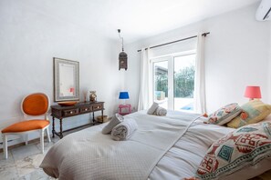 Un dormitorio con una cama grande, una silla, un aparador, un espejo y una ventana con cortinas.