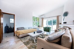 Una sala de estar moderna con un sofá, una mesa de centro y un sill ón verde. Se ve una ventana con cortinas y vistas a la vegetación.