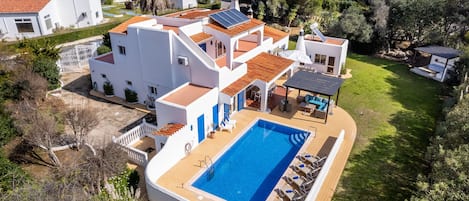 En modern villa med swimmingpool, solpaneler och en välskött trädgård.