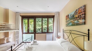Habitació d'hotel amb literes, un gran finestral amb vista a vegetació, un quadre a la paret i un llit ben arropat.
