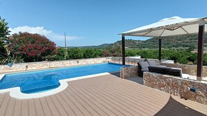 Área da piscina com deck de pedra, espaço coberto para relaxamento e vista para a paisagem ao redor.